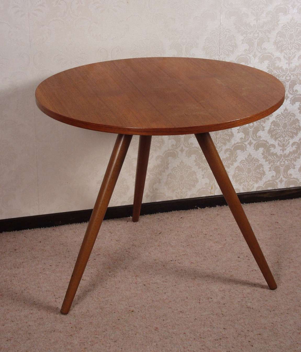 Rundt lite bord i teak med tre ben som skrår ut fra midten av bordplaten.