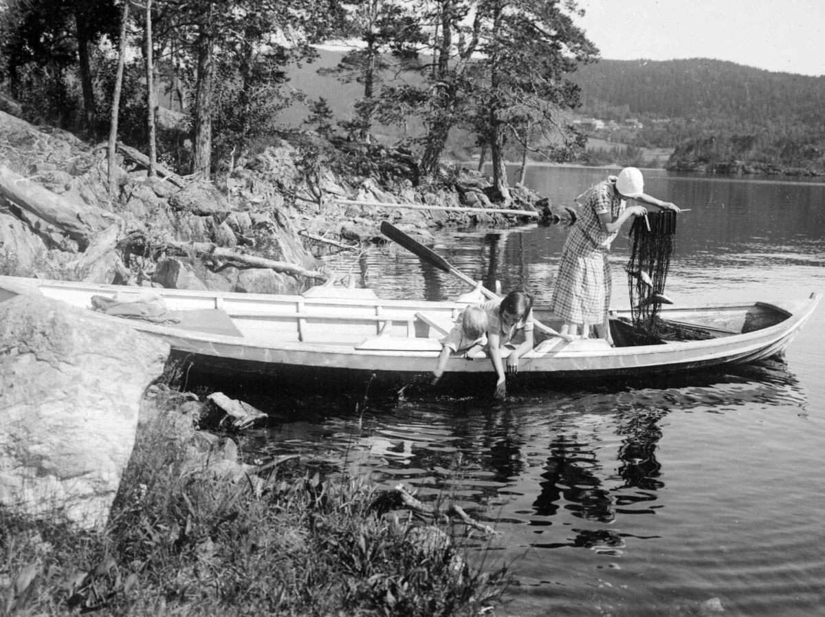 En kvinne, en pike og en gutt i robåt, med fiskegarn, ved Kongeøya.
