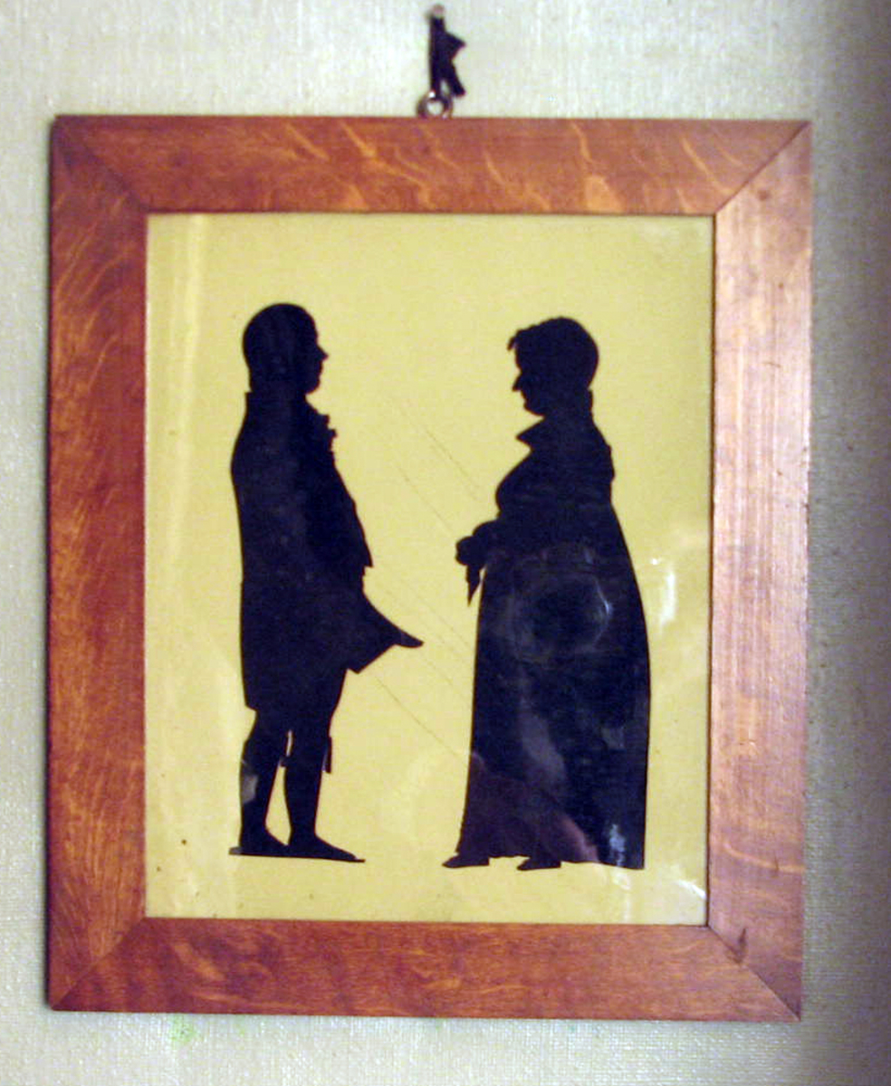 Rektangulær. Mann høyrev., høye støvler, flosshatt i hånden, kv. venstrev., lang kjole m. høyt liv, tørkle i hånden, oppst. krave Drakter fra omkring 1810