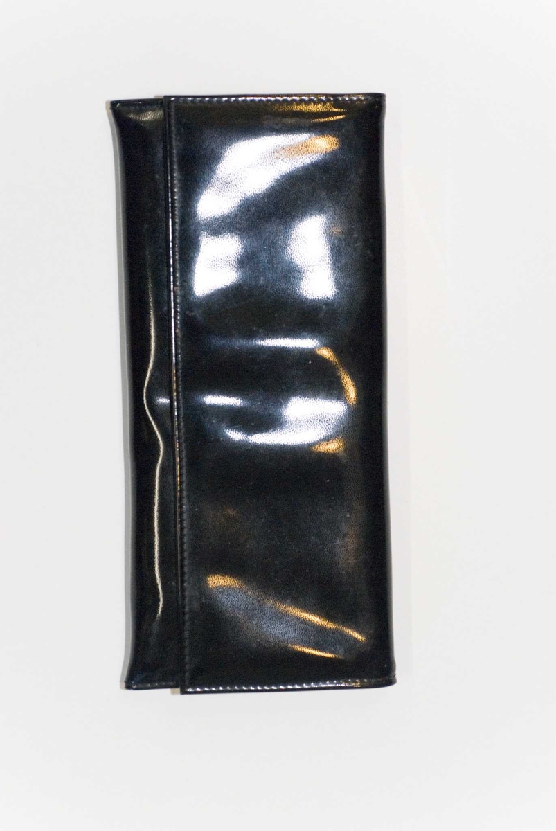Sort konvoluttveske, blankt syntetisk materiale, foret med åpen lomme i foret, lukket med trykknapp.