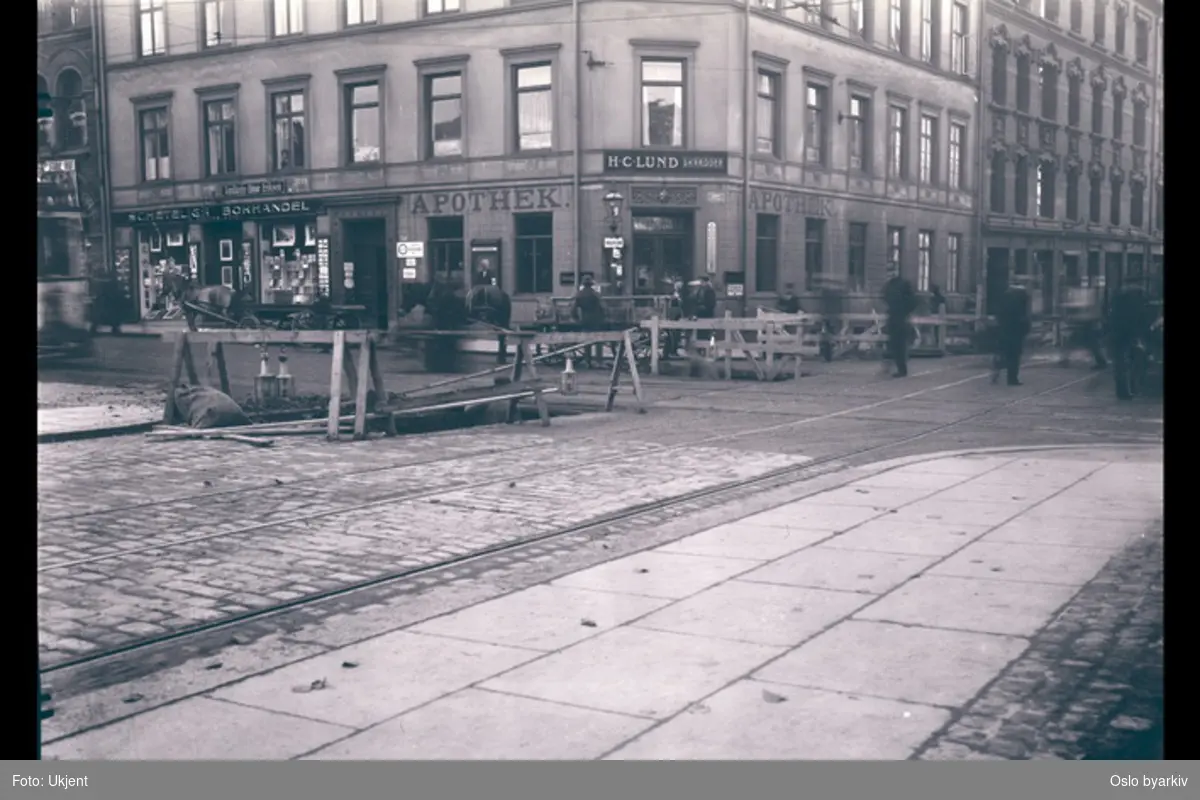 Krysset Rosenkrantz' gate - Stortingsgata. Shetelig bokhandel, H. C. Lund (dame- og herreskredder), apotek, hest med kjerre, gravearbeid i gata.