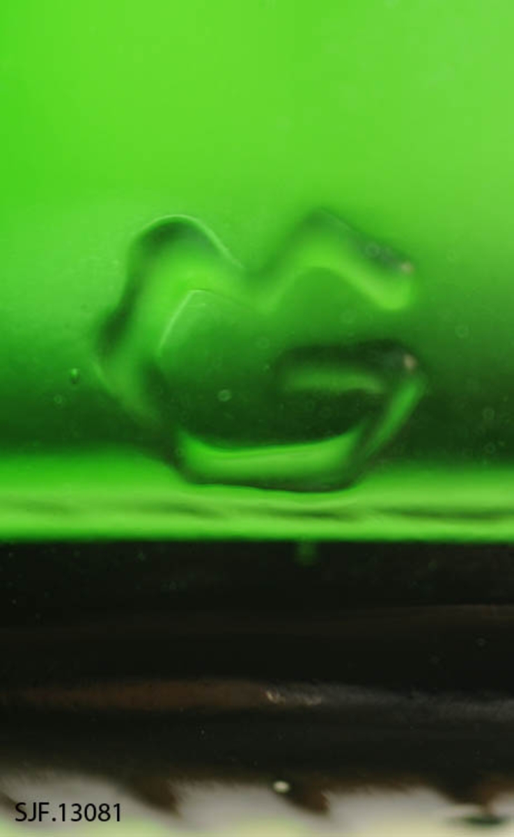 Flasken er av grønt glass, og har en sylindrisk form. Den har flat bunn. 