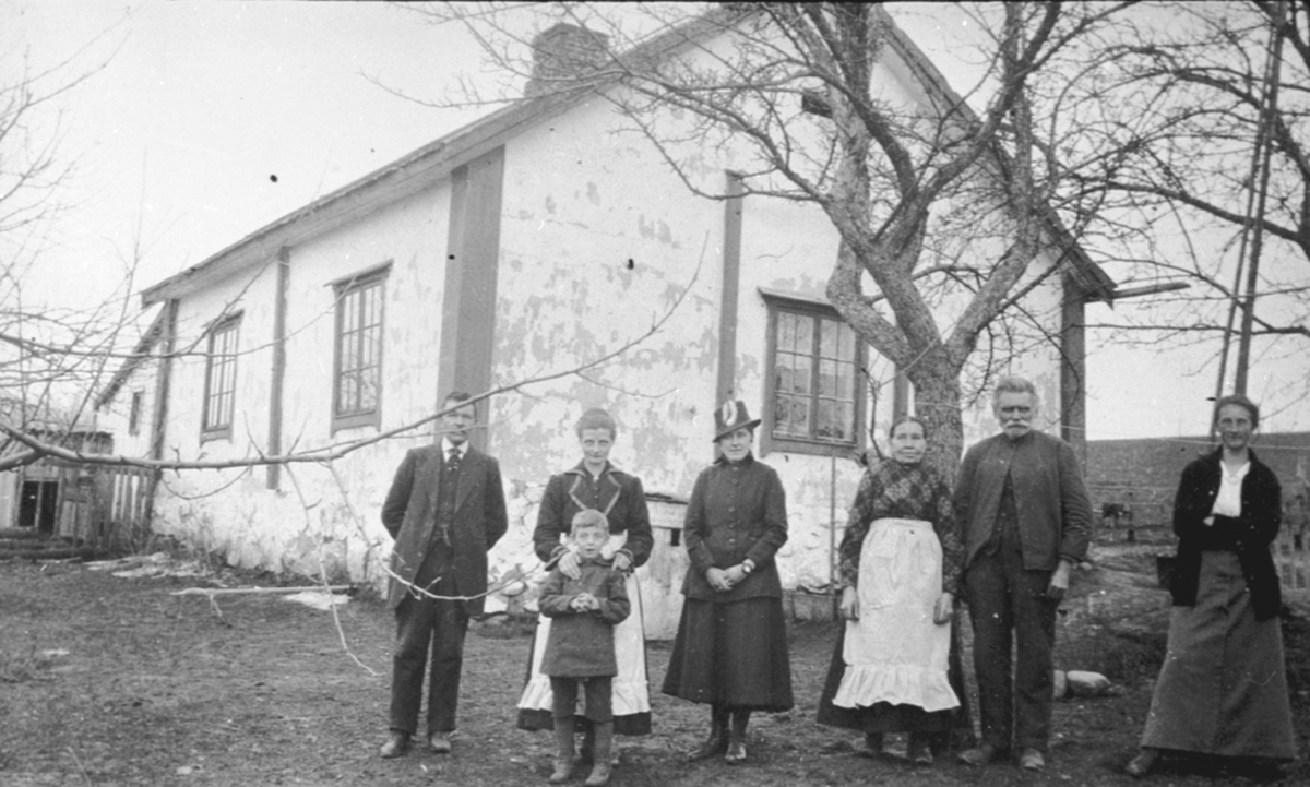 Gruppe personer utenfor huset i Sundby lille, Skredderbakken, Helgøya. Fra venstre er Anders Aas, Guri Aas med sønnen Asbjørn, Hjørdis Aas, Marit Jensdatter, Johannes Akselsen, ukjent.