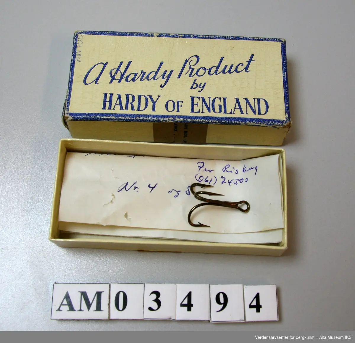 Pappeske med påtrykt "A Hardy Product by Hardy of England" på lokket. 

Inneholder en trippelkrok og en håndskrevet lapp med teksten: 

"Mustad 7228 EBB Superior Nr 1

Mustad 
Per Risberg
(061)74300
Nr 4 og 5"