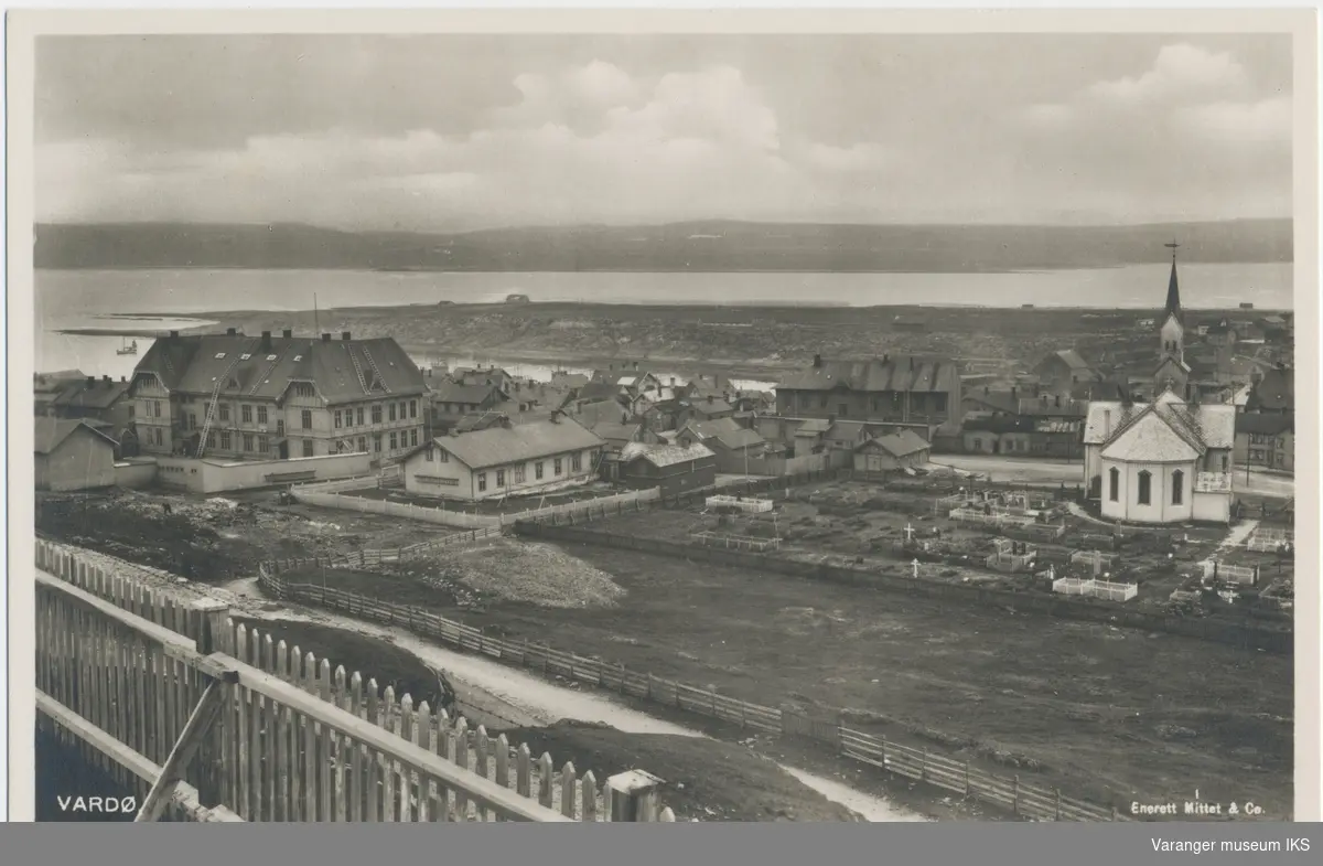 Postkort, byprospekt av Vardø sentrum, kirken og kirkegården i forgrunnen, sett fra Klondyke, Steilneset og fastlandet i bakgrunnen, ca. 1920