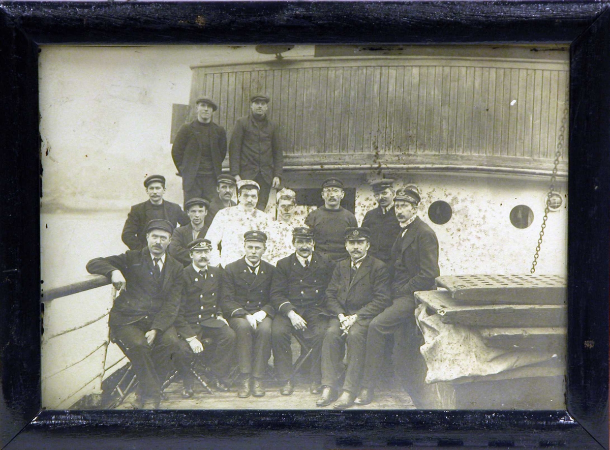 Gruppebilde av mannskap/ besetning på et N.F.D.S. skip poserende på dekk ved rekka foran bruen. 10 stående og 5 sittende.
