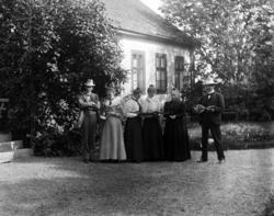 Gruppe kvinner og menn i en hage. Mannen til høyre spiller p