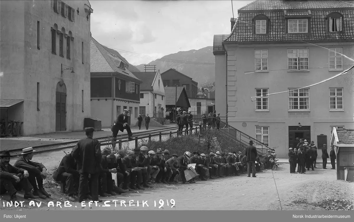 Inntagelse av arbeidere på Norsk Hydro etter streiken i 1919. Arbeidere sitter utenfor kontorbygningen til Norsk Hydro på fabrikkområdet.