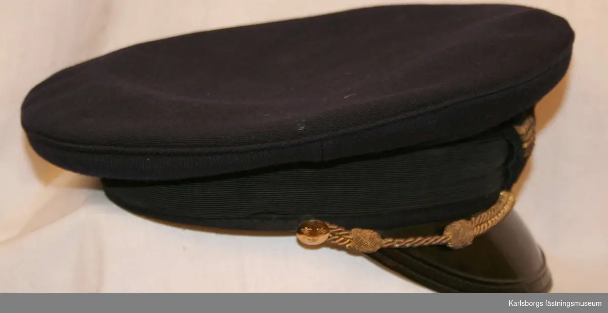 Storlek: 53
Skärmmössa m/1930  av mörkblått tyg, mössband av svart räfflat silke, svart lackerad skärm. Försedd med rund guldsnodd som hakrerm fäst vid  2 st 14 mm uniformsknappar samt flygemblem.