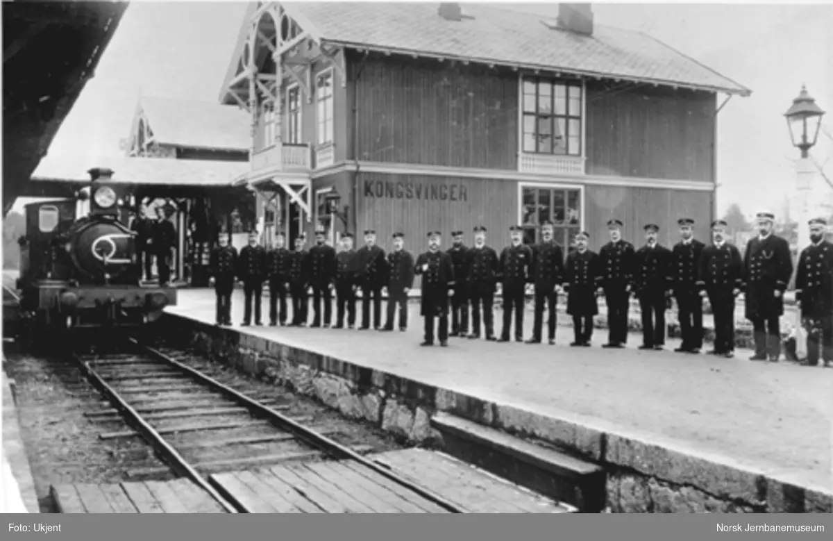Personalet på Kongsvinger stasjon oppstilt foran stasjonsbygningen og med et damplokomotiv i spor 1