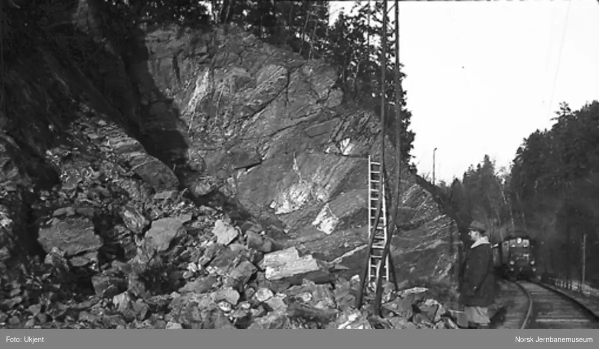 Arbeid med forskjæring til tunnel, ev. bortsprenging av fjell på dobbeltsporanlegget Sandvika-Asker; tog passerer