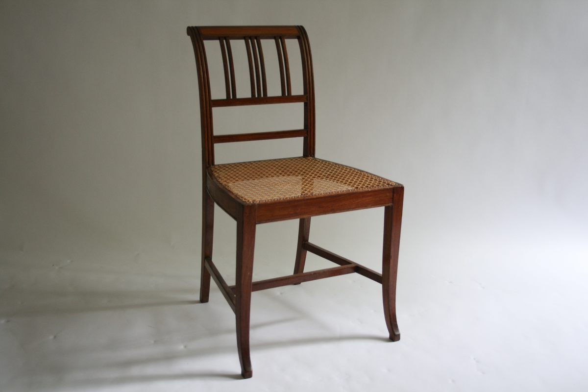Spinkel stol i mahogni, med rottingsete, smale spiler i ryggen. 5 stoler og 1 kanapé.