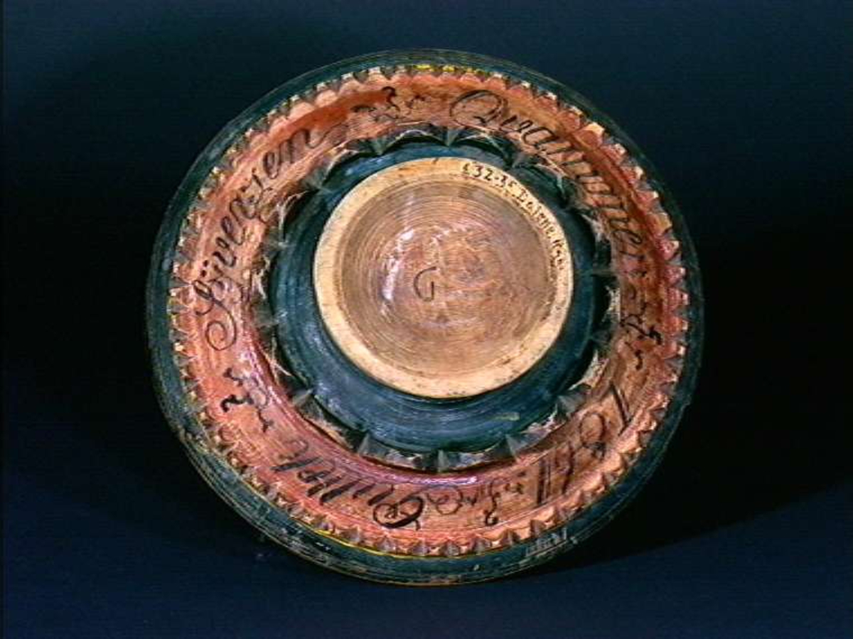 Furu, dreiet, utvendig grønnmalt med lyserødt, fot cirkelformet, skrå sider, dreiet, avsatser med skårne takkekanter, malt : "Gullek Syversen Qvammen 1861" Under fot skåret "G".