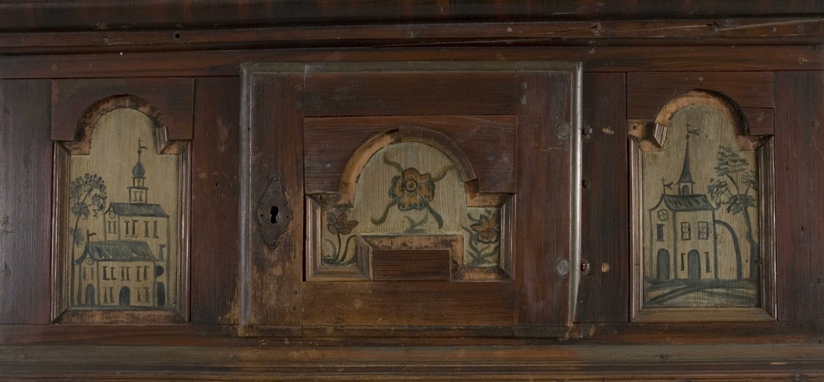 Framskap i en del med en dør nede, en  oppe og en liggende i midten. Dørene har malte blomstermotiver mens de 8 sidefeltene har malte bygninger.