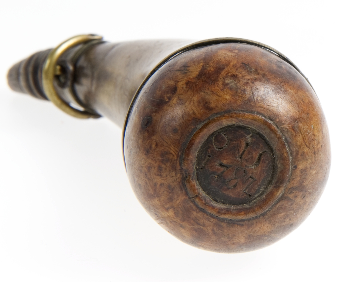 Krutthorn med skålformet bunn i tre med innskrift og beslag i messing. Risset ornamentikk på horn i form av akantusblader og dyr.