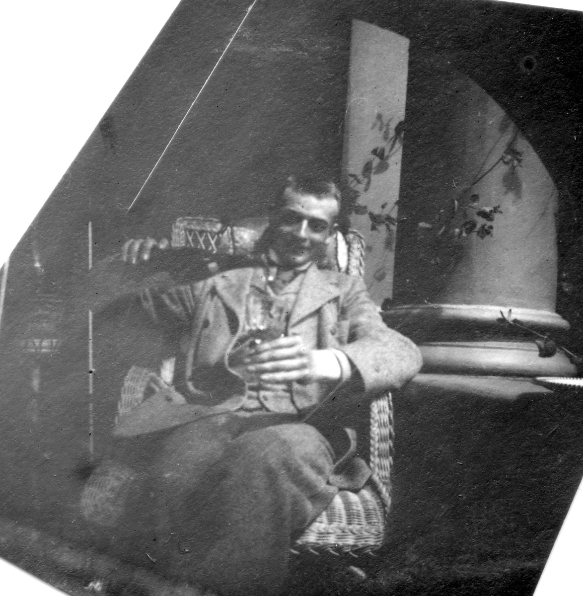 Portrett av Jacob Alver, sittende i kurvstol med glass i hånda.