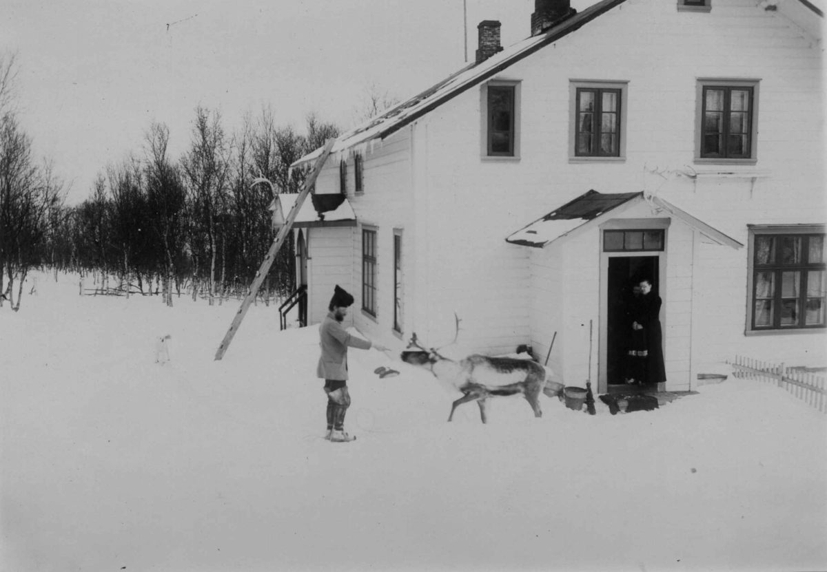 To personer og et reinsdyr utenfor legeboligen Solheim hvor Dr. Andreas B. Wessel og Ellisif Wessel bodde. Kirkenes, Sør-Varanger, Finnmark, 1899. Kvinne står i døren.