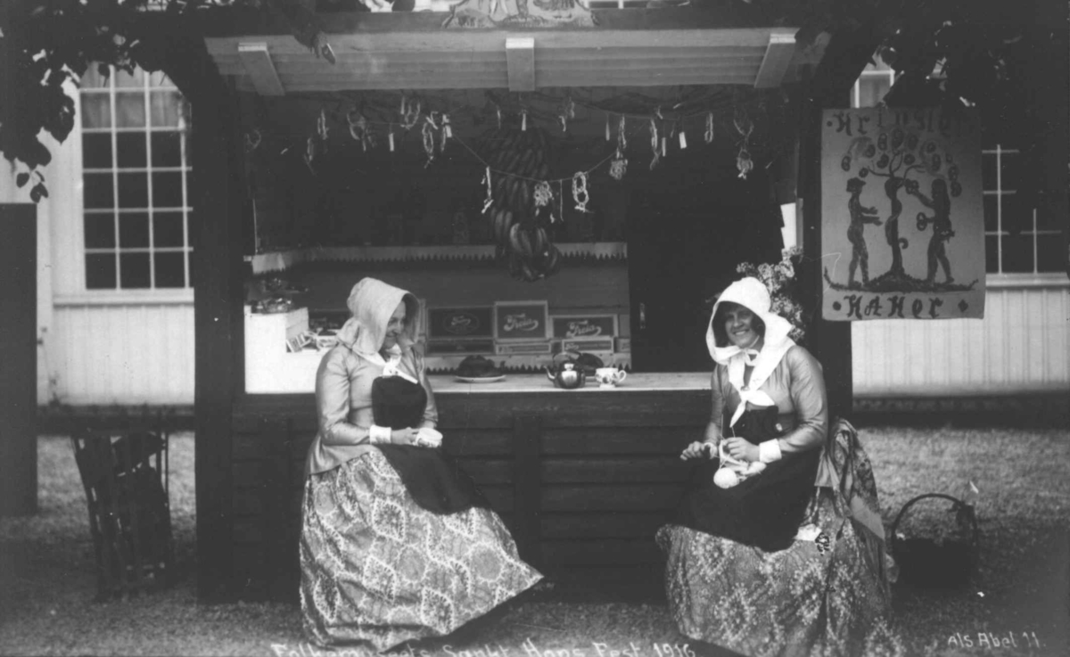 St. Hans fest på Norsk Folkemuseum i 1916. Kvinner med hatter og håndarbeid foran salgsbod.