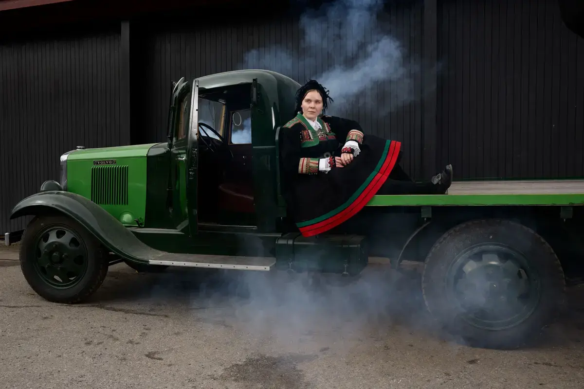 Woman in traditional bunad costume sitting in an old truck with smoke effects during the Easter mystery event at Norsk Folkemuseum.